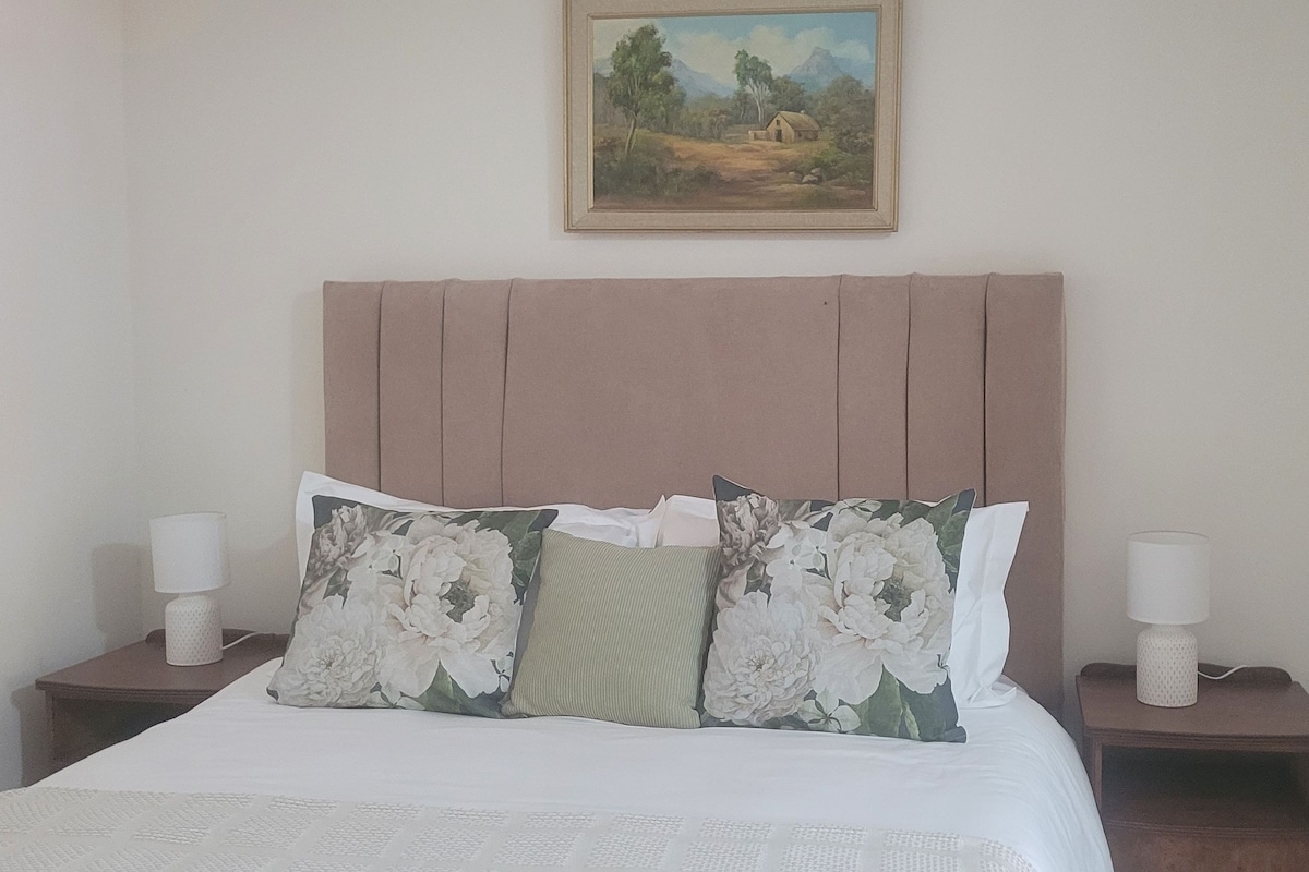 A bed with a headboard, two bedside tables with lamps, and a painting on the wall.