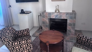 A living room with a fireplace, a television mounted on the wall, and patterned sofas. - On Guest Av (Harare)