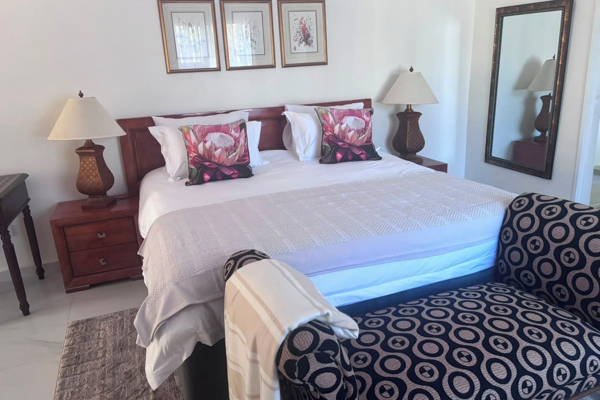 A hotel room with a bed, two bedside tables with lamps, a patterned sofa, and a large mirror on the wall.