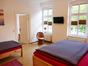 Ein Schlafzimmer mit zwei Betten, einem Sessel, einem Fernseher und einem Fenster mit Jalousien.