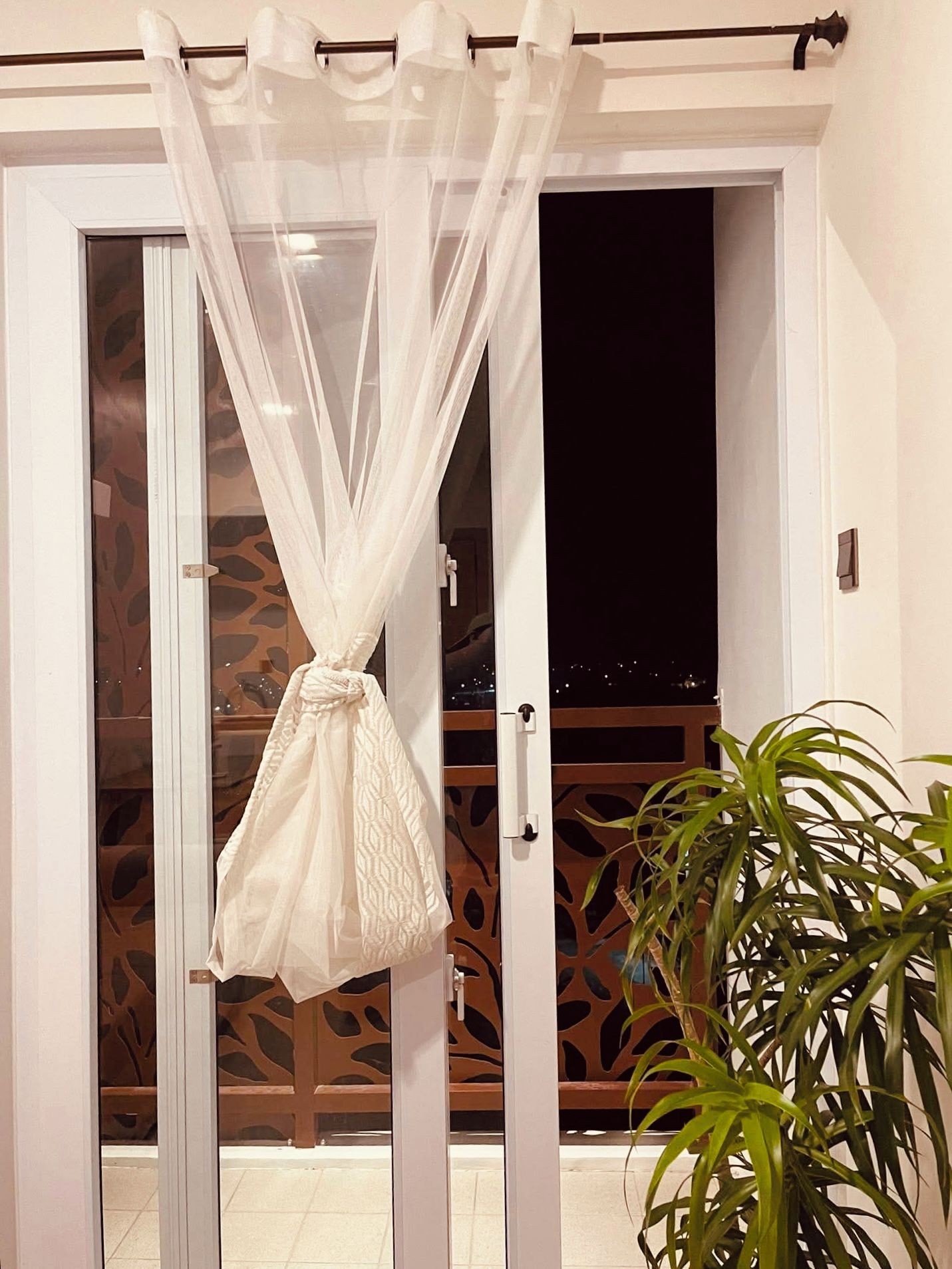 Une pièce dotée d’une porte-fenêtre coulissante, d’un rideau blanc et d’une plante en pot.