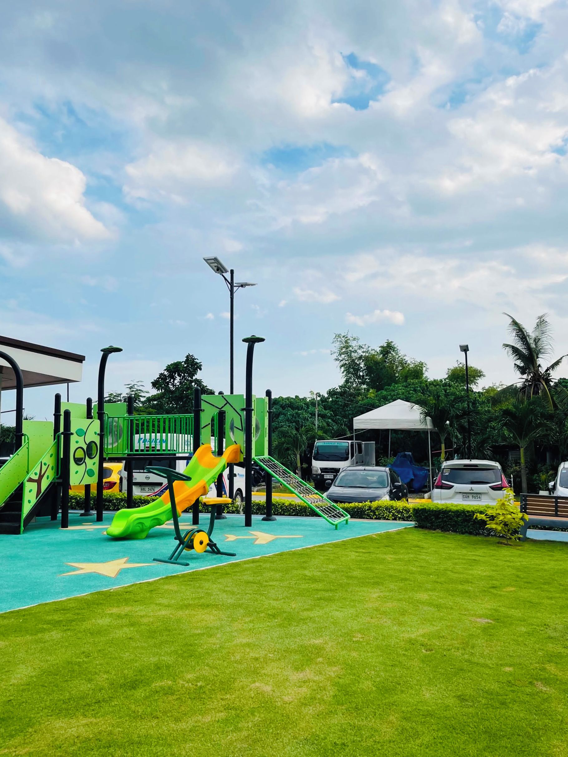 A playground with slides and climbing structures, surrounded by grass and trees.
