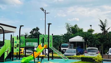 A playground with slides and climbing structures, surrounded by grass and trees.