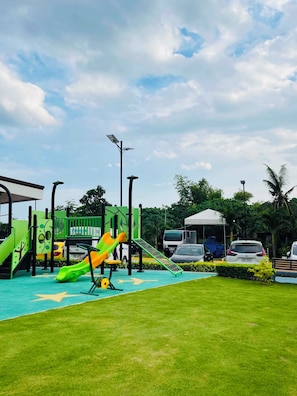 Un parque infantil con toboganes y estructuras para escalar, rodeado de césped y árboles.