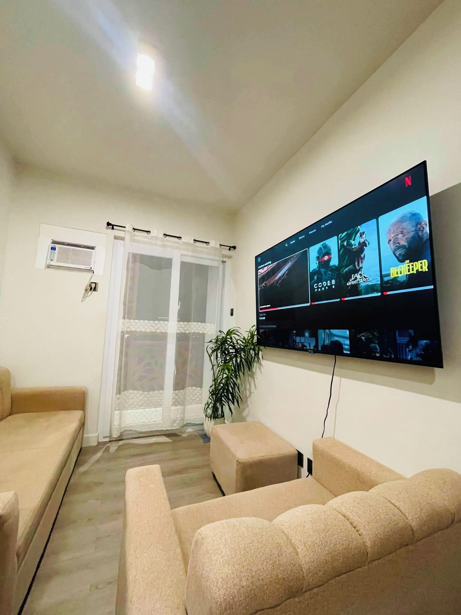 A living room with a flat-screen TV mounted on the wall displaying multiple movie options.