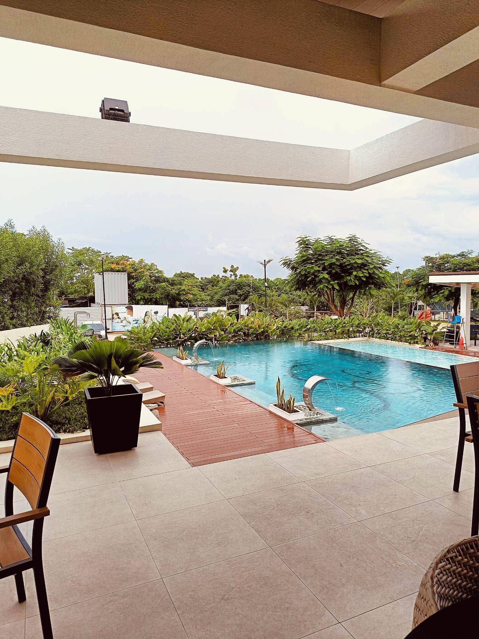 A pool area with a tiled deck, lounge chairs, and a view of the surrounding greenery.