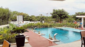 A pool area with a tiled deck, lounge chairs, and a view of the surrounding greenery.