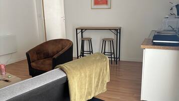 A modern living space with a sofa, a small table, a kitchen area, and a poster on the wall.