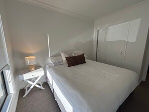 Quarto com cama, mesa de cabeceira, abajur e guarda-roupa.