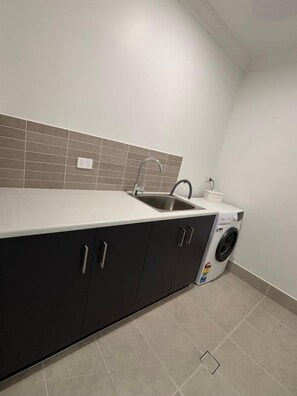 Uma cozinha compacta com pia, armários escuros, máquina de lavar e painel de azulejos.