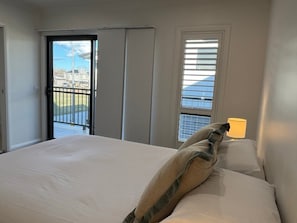A hotel room with a bed, a window with blinds, a door leading outside, and a lamp on the bedside table.