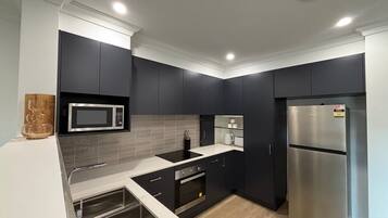 A modern kitchen with dark cabinets, stainless steel appliances, and a white countertop.