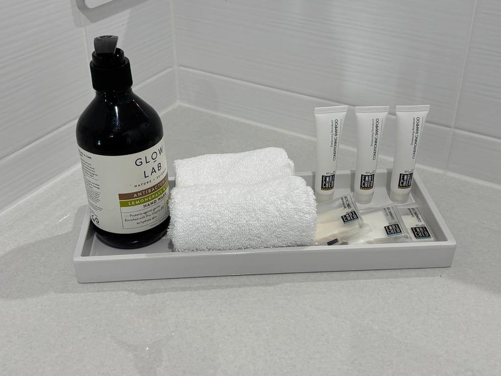 Una encimera de baño con una botella de jabón de manos Glow Lab, una toalla blanca y varios tubos de crema para manos.