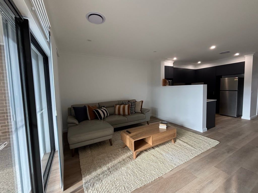 A modern living room with a sofa, coffee table, and a kitchen area in the background.