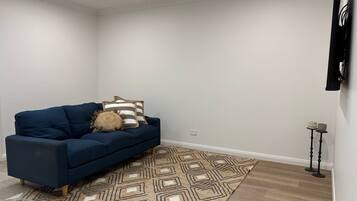A room with a blue sofa, patterned rug, and a wall-mounted TV.