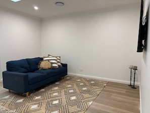A room with a blue sofa, patterned rug, and a wall-mounted TV.