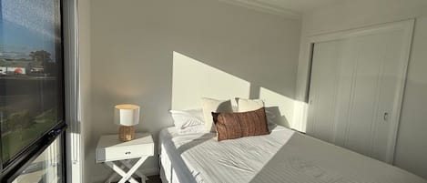 A hotel room with a bed, a nightstand, a lamp, a window, and a door.