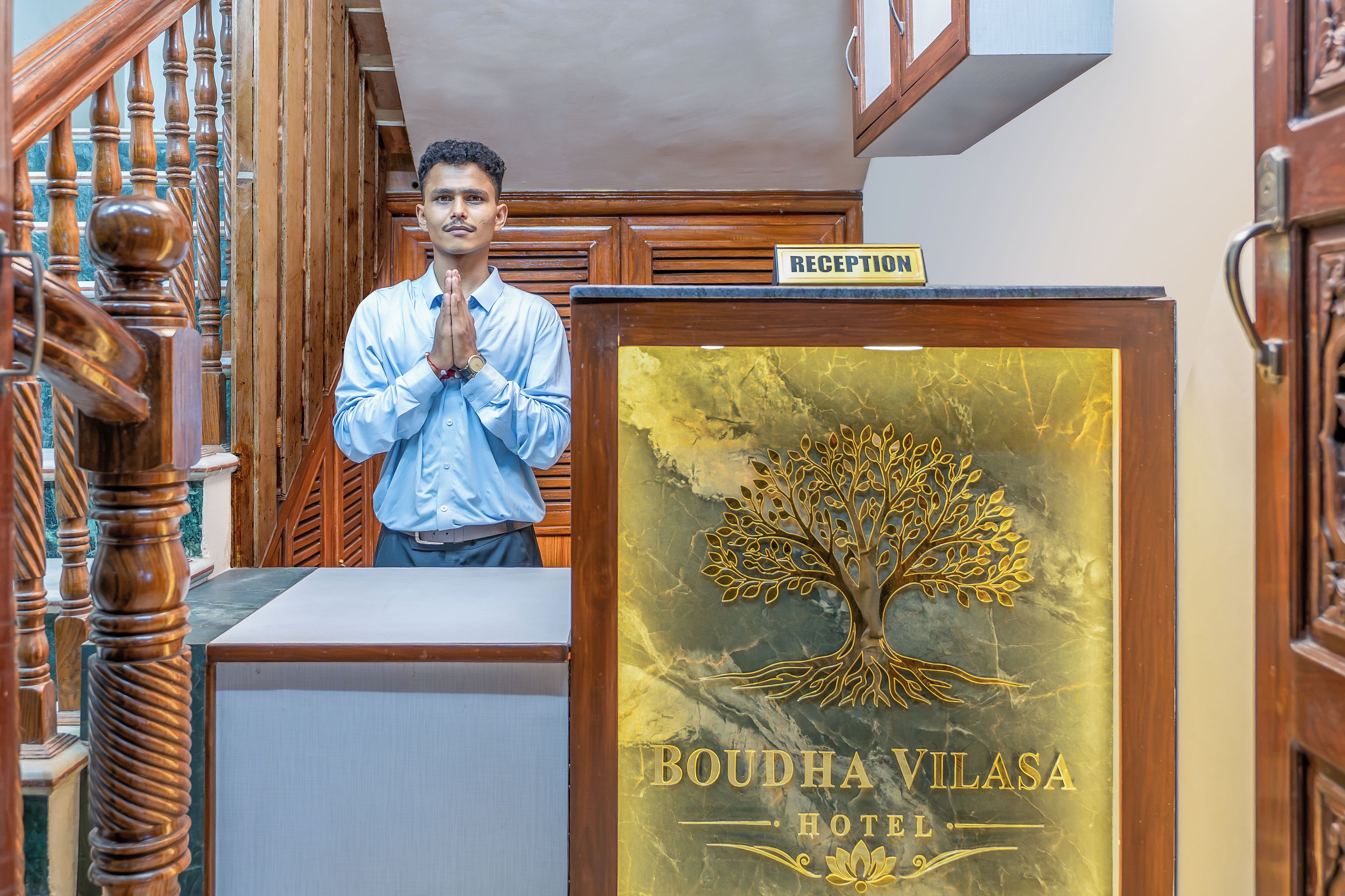 Un comptoir d’accueil avec une enseigne indiquant « HÔTEL BOUDHA VILASA » et un emblème représentant un arbre.