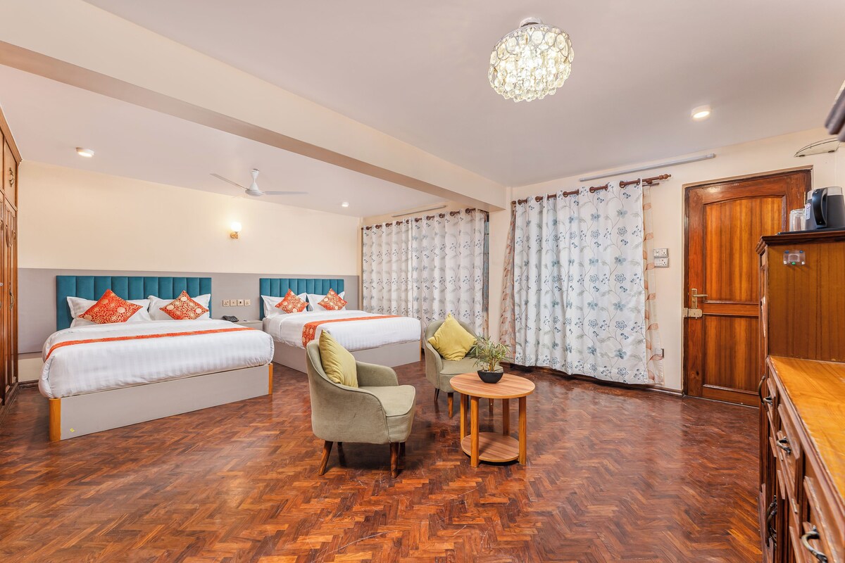 Habitación de hotel con dos camas, una zona de estar, una araña y un armario de madera.