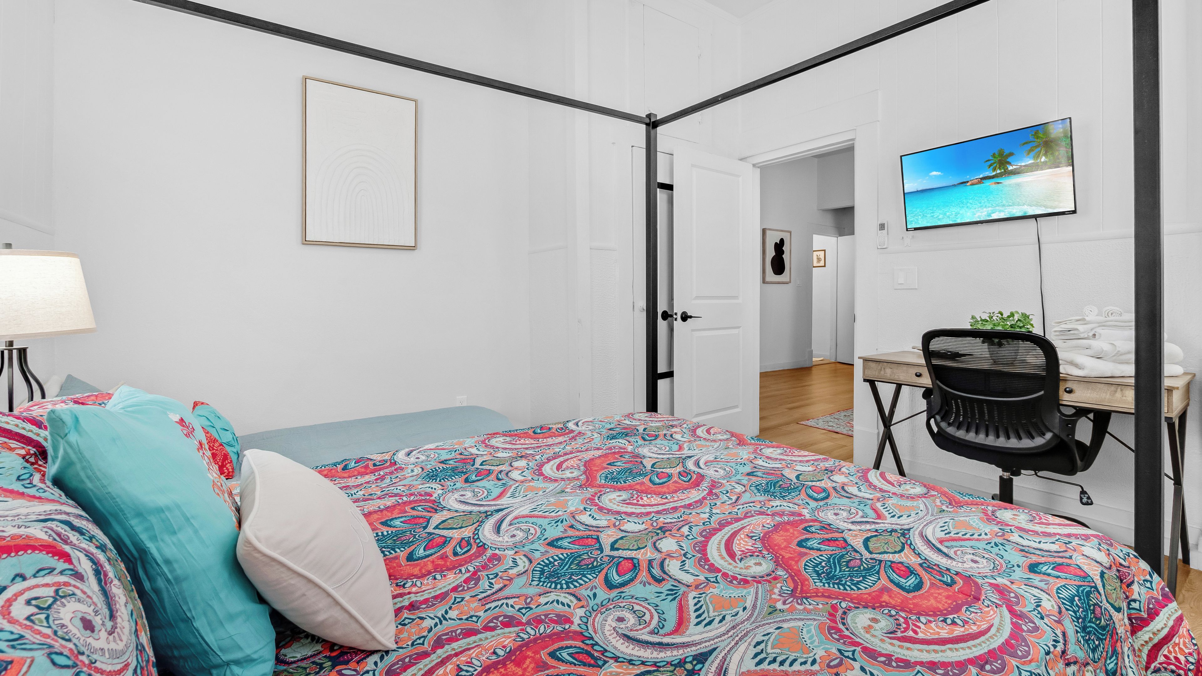 A bedroom with a bed, a desk, and a television.