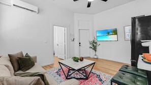 A modern living room with a sofa, a coffee table, a TV, and a refrigerator. - Tobin Hill Apt. Walk to The Pearl & St. Mary Strip (San Antonio)