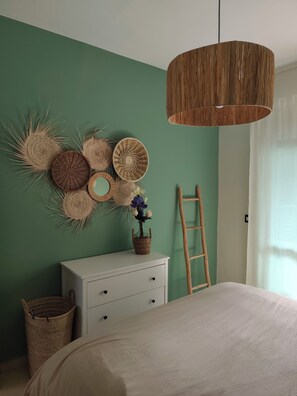 Ein Schlafzimmer mit einem Bett, einer weißen Kommode, einem gewebten Wandbehang und einer Holzleiter.