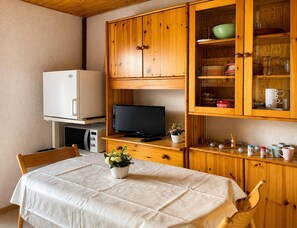 Eine kleine Küche mit Holzschnitzern, einem weißen Kühlschrank, einem Fernseher und einem Esstisch mit weißem Tischlein.