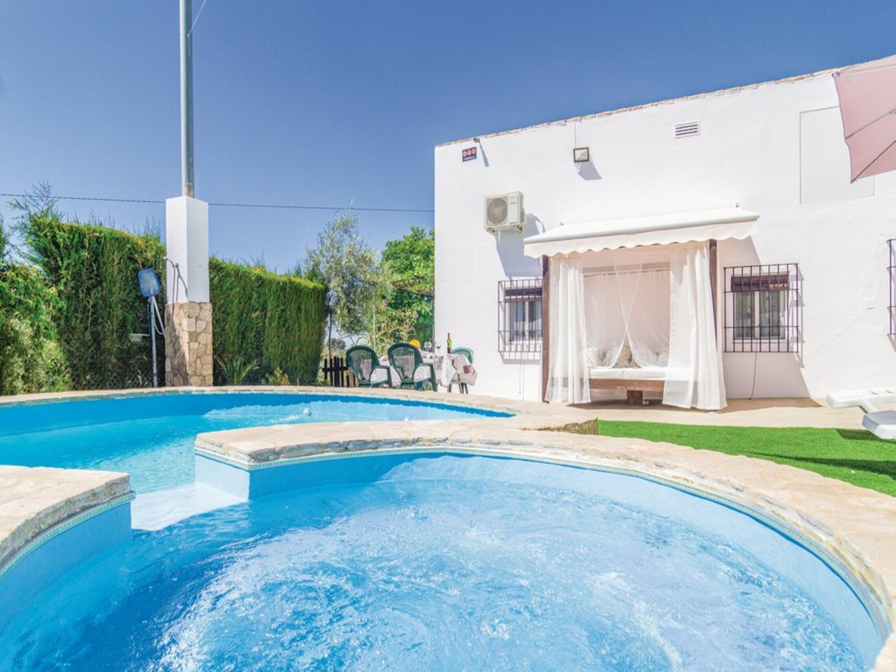 Una piscina amb un edifici blanc a prop, amb una zona d'estar coberta a l'aire lliure i un petit jardí.