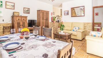 Zona de menjador amb taula preparada per a quatre, un sofà i una televisió al fons.