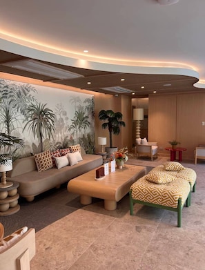 A modern lounge area with a sofa, armchairs, a coffee table, and a mural of tropical plants. - The Base Rise Condo Phuket Middle of The Island (Wichit)