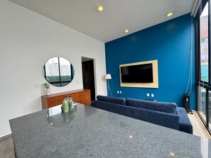Ein moderner Wohnraum mit Kücheninsel, einem großen Flachbildfernseher an einer blauen Wand und einer Sitzecke mit blauen Sofas.