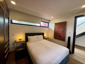 Ein Hotelzimmer mit Bett, Nachttischlampen, Wandteppich und Fenster mit Blick.