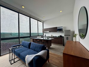 Ein modernes Interieur mit einer Couch, einer Küche und großen Fenstern.