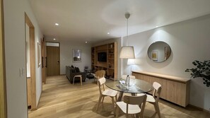 Ein modernes Wohnzimmer mit einem Glastisch, Holzstühlen, einer Couch und einem an der Wand befestigten Fernseher.