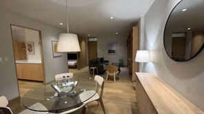 Ein modernes Hotelzimmer mit einem Glastisch, einer Couch, einem Sessel, einem Bett und einem großen Spiegel.