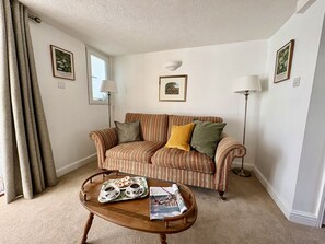 A living room with a striped sofa, a coffee table with a tray of pastries, and two framed pictures on the walls. - Crowfoot Cottage -  Stratton, Dorchester (Stratton)