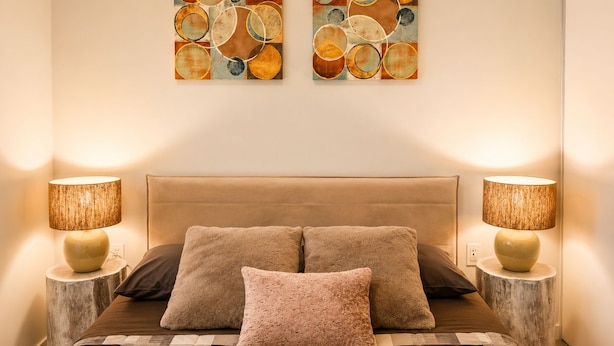 Een slaapkamer met een groot bed, twee wandlampen en twee abstracte schilderijen.