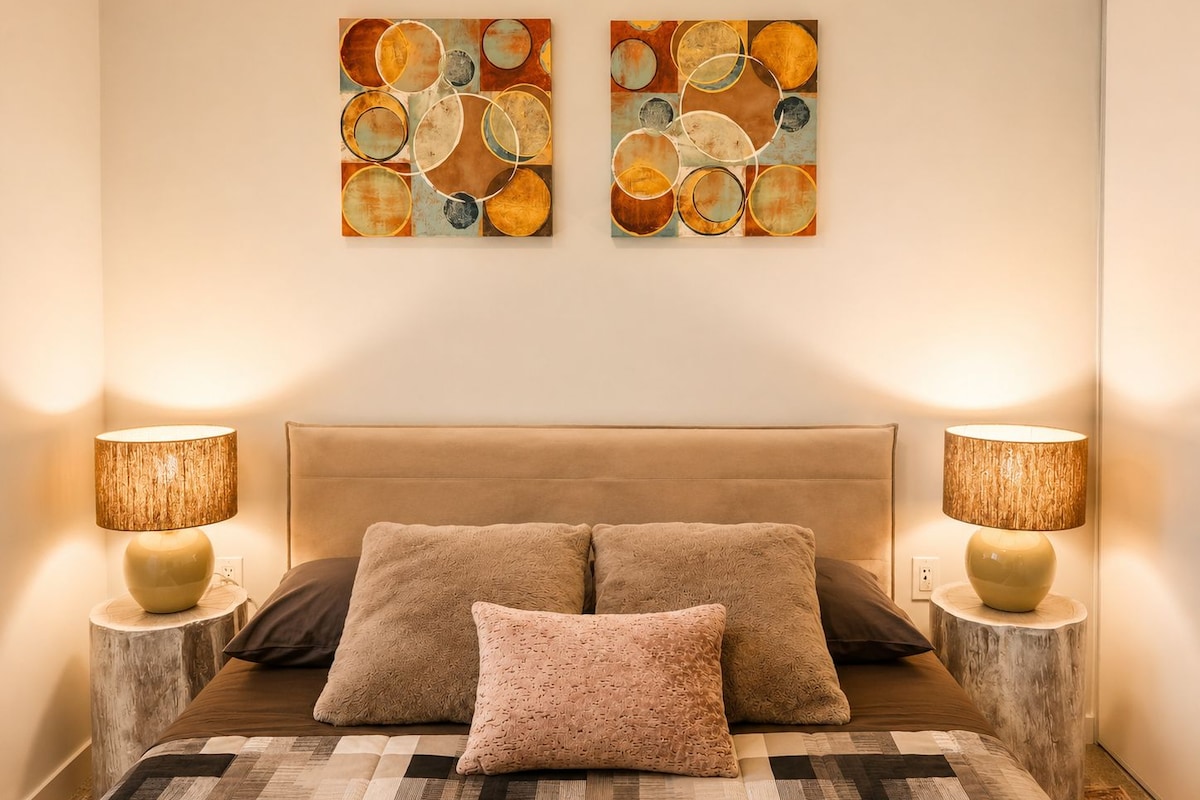 Un dormitorio con una cama grande, dos lámparas de pared y dos cuadros abstractos.