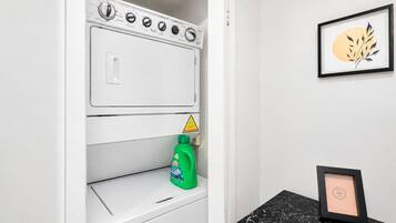 Uma lavanderia com máquina de lavar, um frasco de detergente e um quadro em cima do balcão.