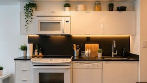 Een moderne keuken met witte kasten, een magnetron, fornuis en vaatwasser.