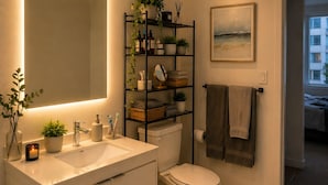 Een moderne badkamer met een grote spiegel, een witte wastafel en toilet. Er is een plankje met toiletartikelen en een schilderij aan de muur.