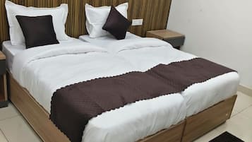 Una cama bien hecha con ropa blanca y marrón, un cabecero de madera y un tapete negro sobre un suelo de baldosas.