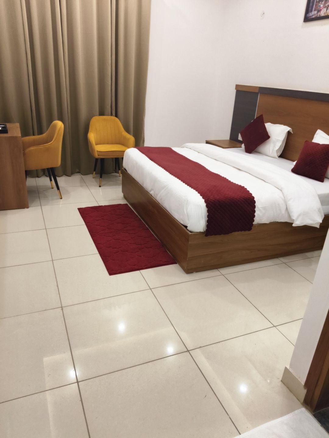 A hotel room with a bed, two chairs, a desk, and a red rug.