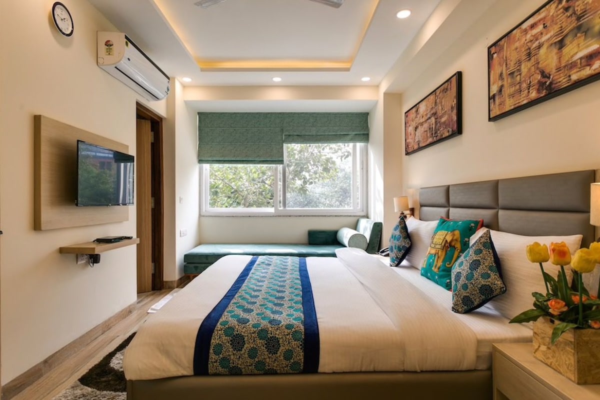 A hotel room with a bed, a television, a window with a view, and artwork on the walls.