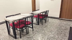 Una habitación con dos mesas y cuatro sillas, cada una con cojines rojos. El suelo presenta un diseño de baldosas con vetas.