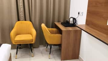 A small, modern room with a bed, two yellow chairs, a wooden desk, and a coffee maker.