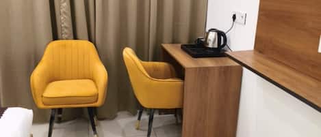 A small, modern room with a bed, two yellow chairs, a wooden desk, and a coffee maker.