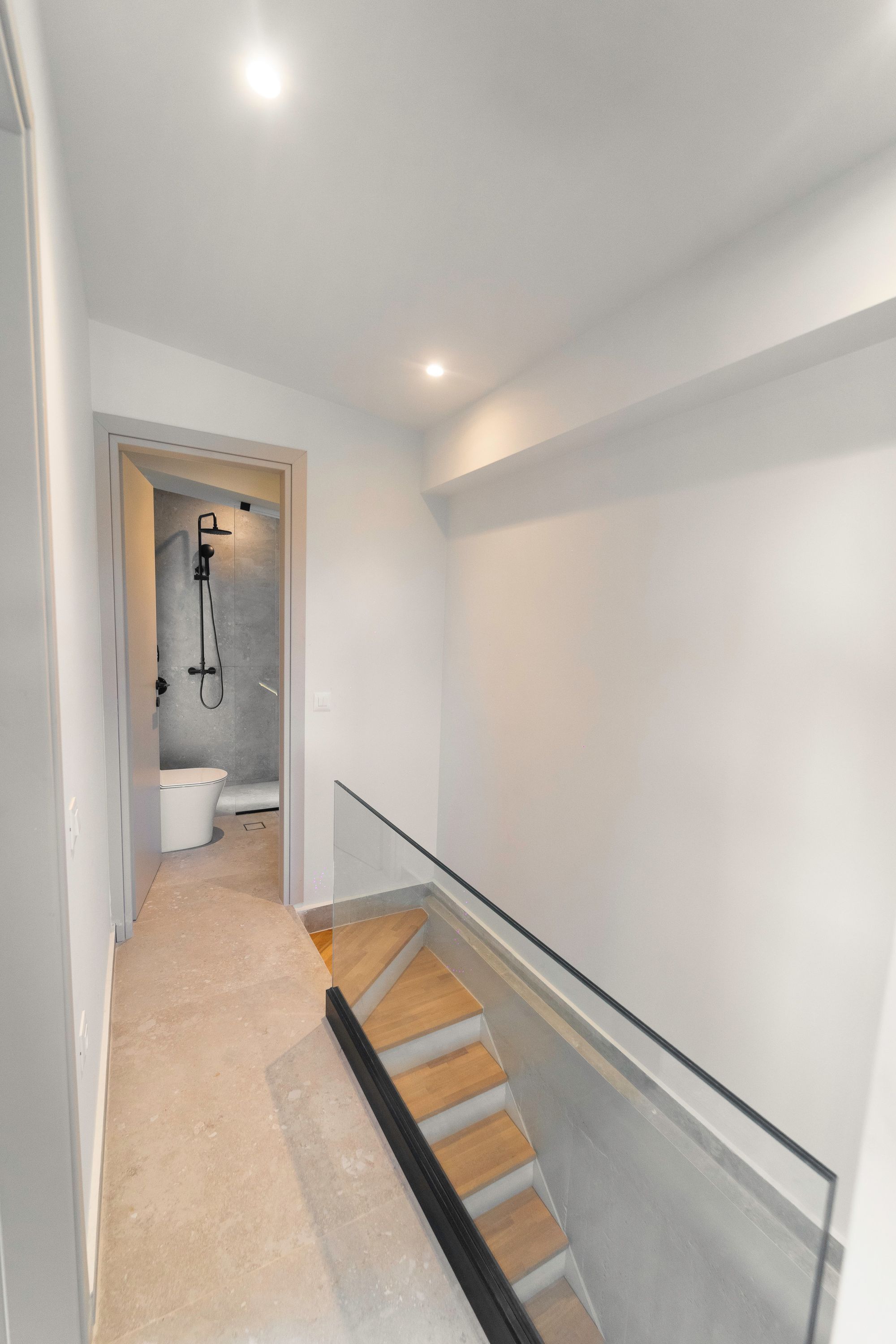 Un couloir étroit avec une rambarde en verre et un escalier en bois.
