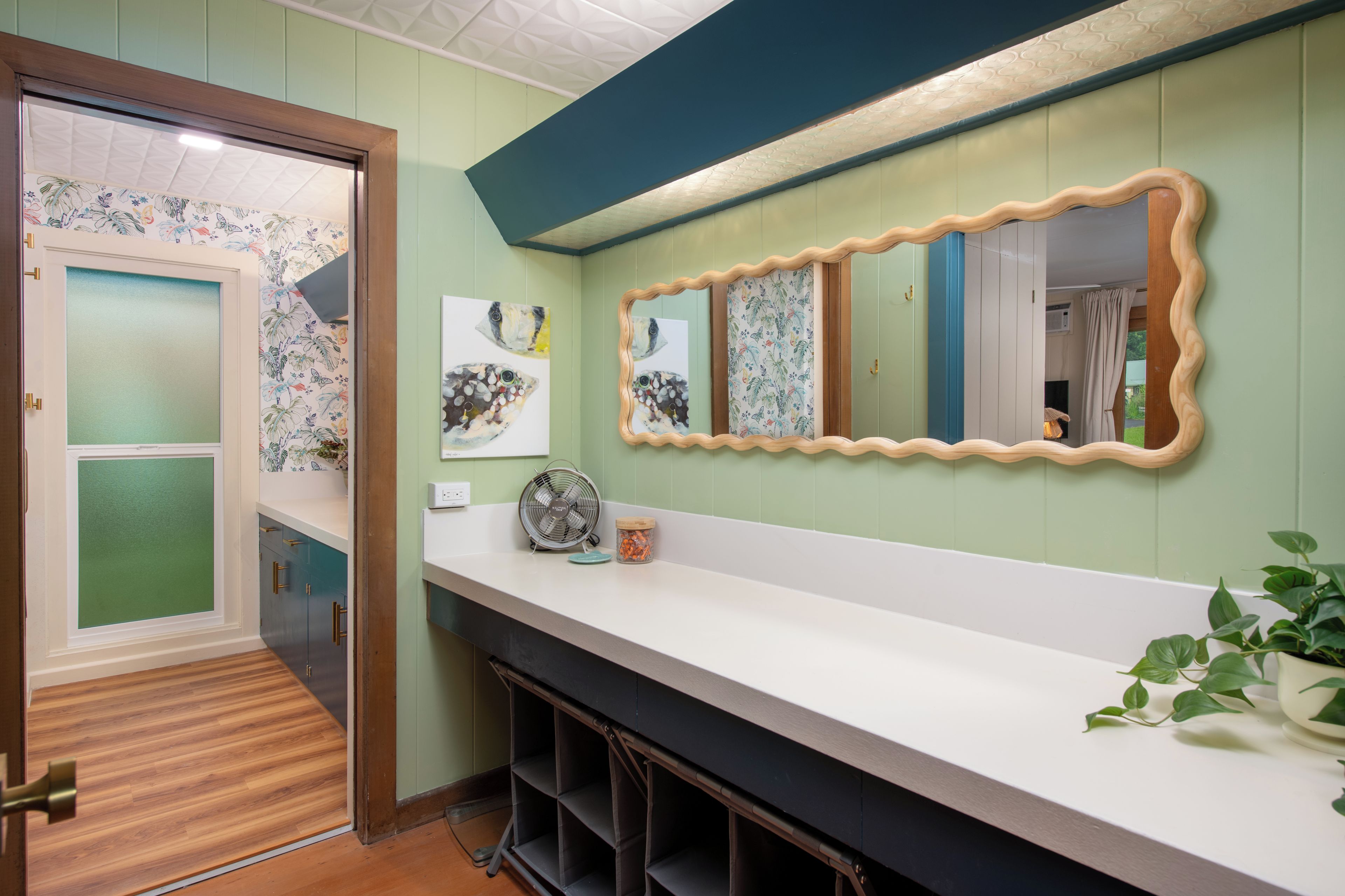 Une salle de bain moderne avec un comptoir blanc, un grand miroir et un ventilateur.