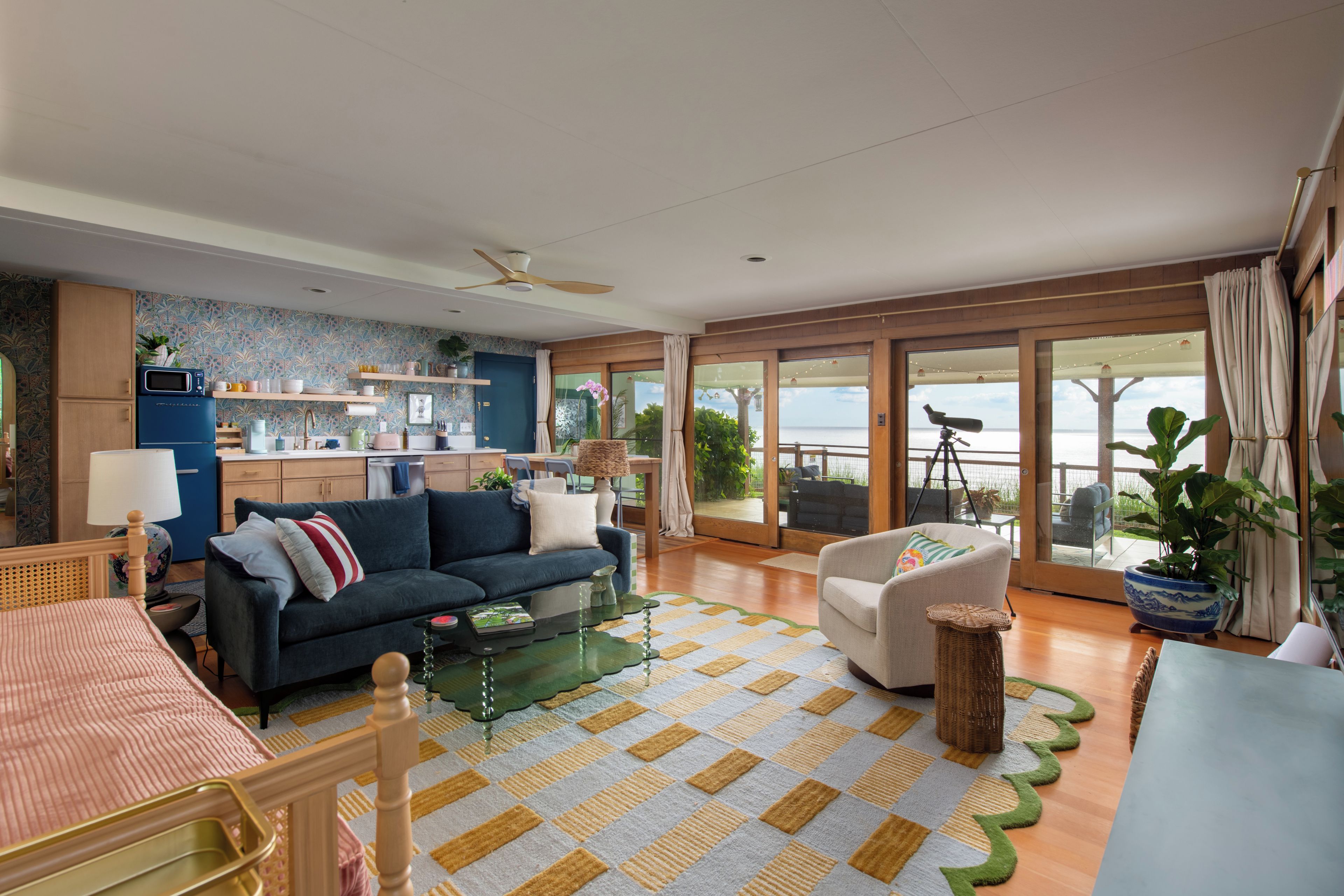Een ruime zithoek met een bank, fauteuil en een eettafel. In de achtergrond is een keuken te zien, en er is een balkon met uitzicht.